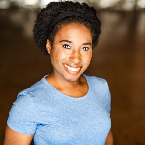 Alicia Plummer smiling, in front of a brown background.