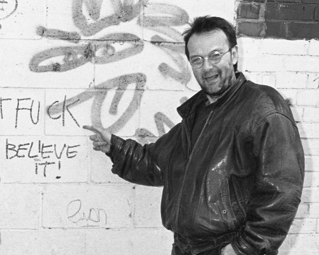 David Fennario pointing at graffiti on a brick wall.