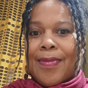 A photo of Heather Cherron von Atzigen staring forward and smiling in front of a yellow and brown background.