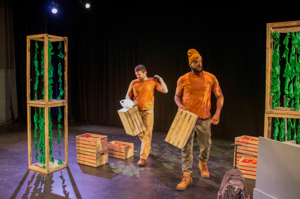 A photo of the "Harvest Justice" production showing two people carrying tomato crates.