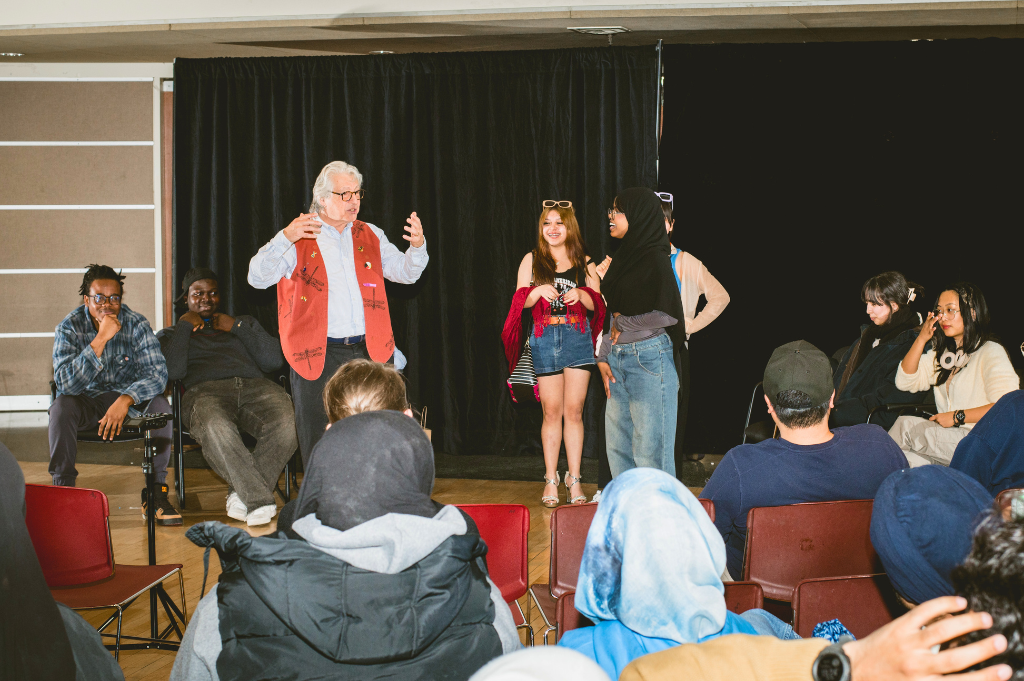 A photo of a facilitator talking to youth onstage during a theatre production.