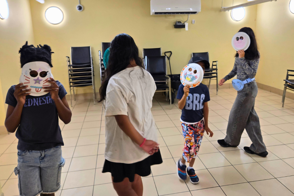 A group of youth wearing decorated paper plate masks participating in a theatre workshop.
